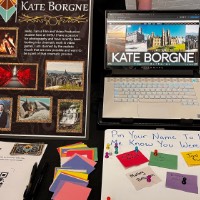White board that says "Pin your name to let me know you were here!" with colorful paper held on with a magnet at Kate Borgne's table.